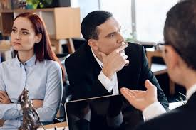 Young divorcing couple looks in different directions, listening to lawyer who sitting at table.