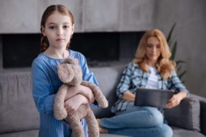 Sad girl holding her teddy bear while her mother is busy.