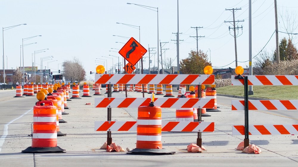 Orange barrels, barricades, and signs blocking a road.