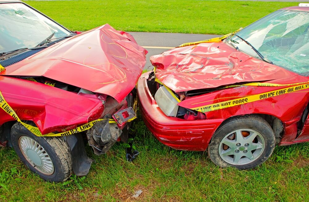 Head on collision of two red cars both with cracked windshields and smashed hoods.