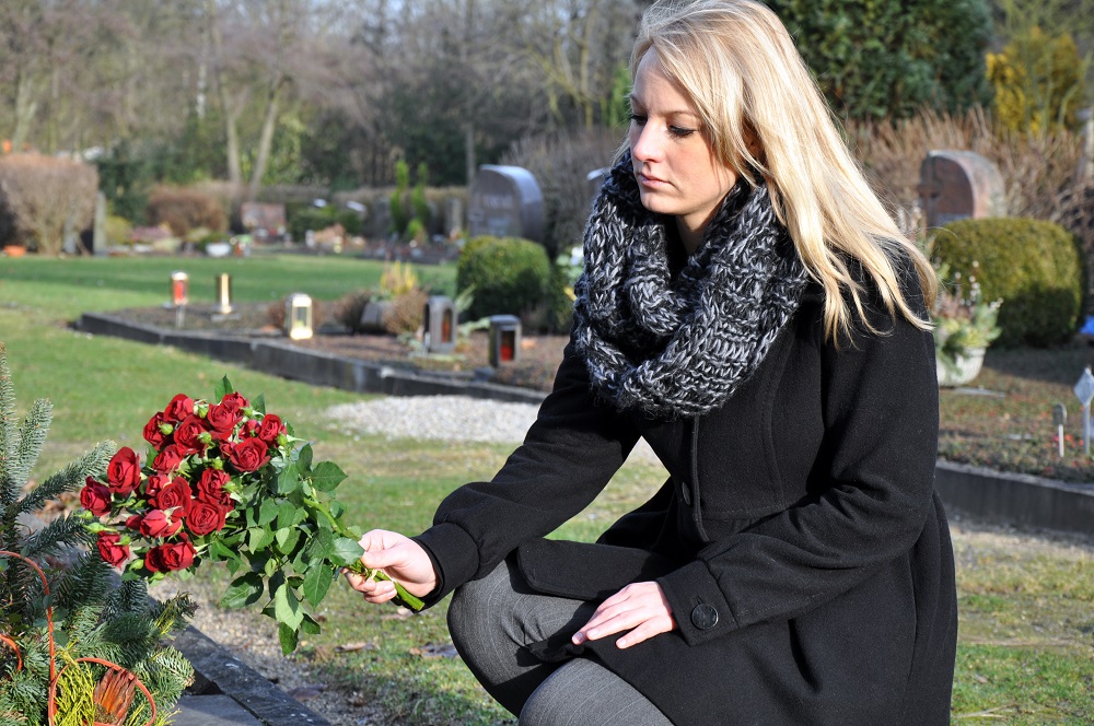 Sad woman offering flowers in the cemetery.