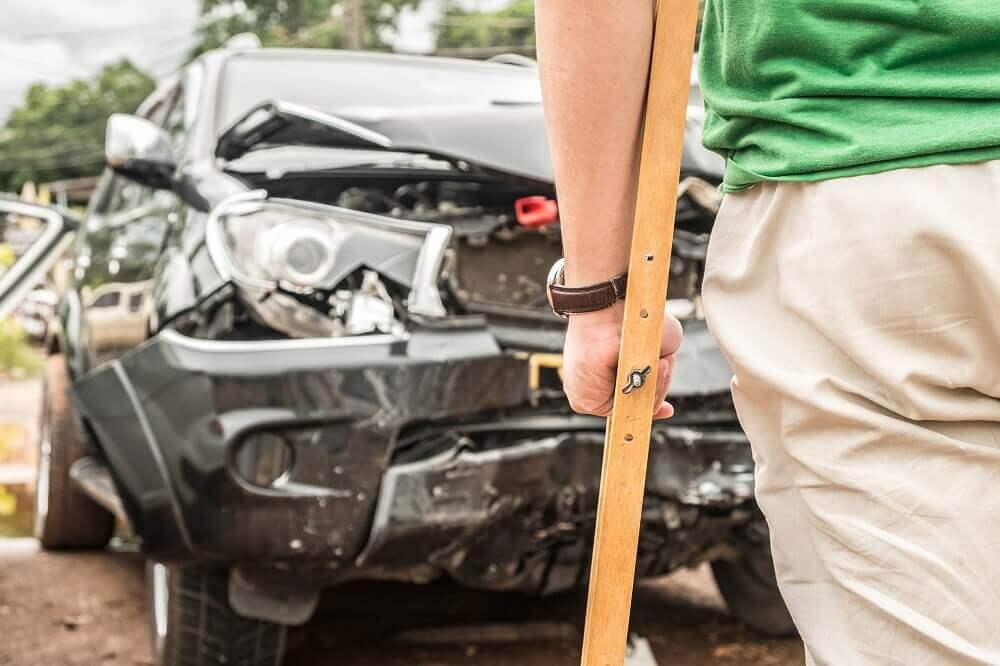 Injured driver on crutches facing at his damaged car.