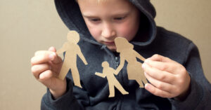 Young boy staring at broken family paper doll.