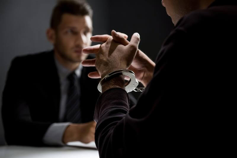 Criminal man with handcuffs being interviewed in interrogation room after committed a crime.