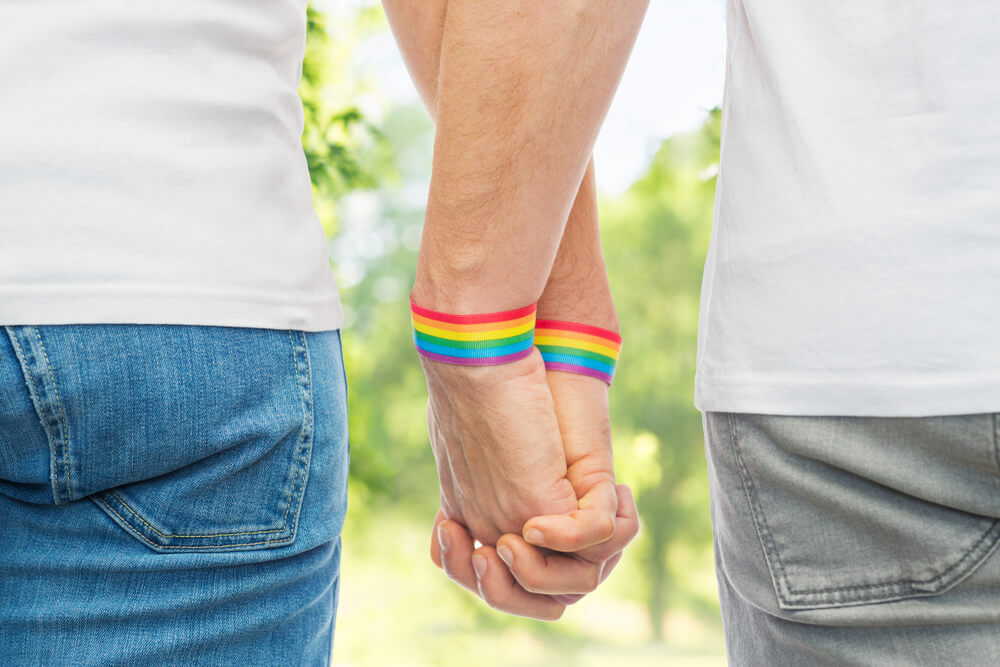 Male couple wearing gay pride rainbow awareness wristbands holding hand.